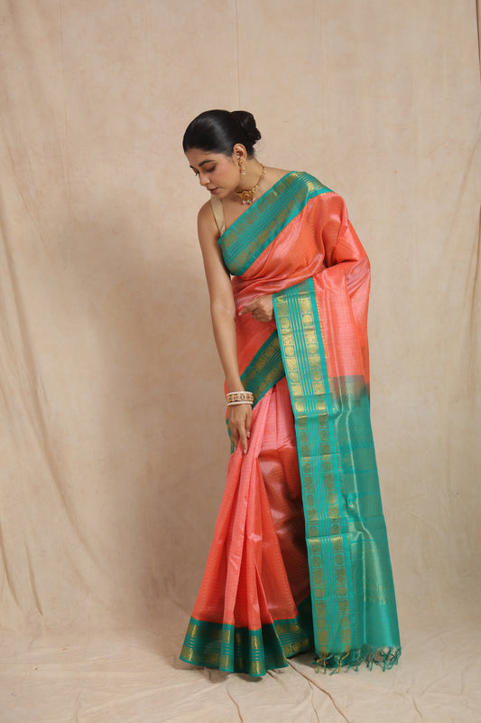 Coral peach Kanchipuram Sico saree with aqua green border, elegant traditional saree by Joyee Kolkata, draped in a graceful pose.