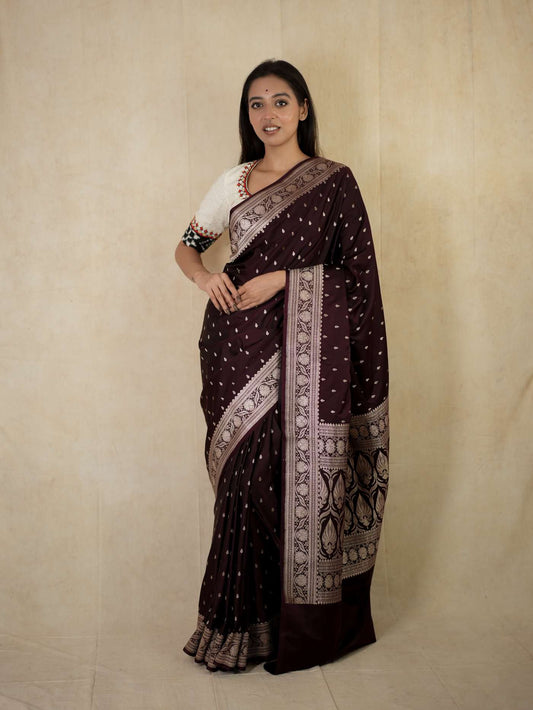 Dark brown Benarasi semi-silk saree with intricate zari work and matching blouse piece, displayed on a hanger.