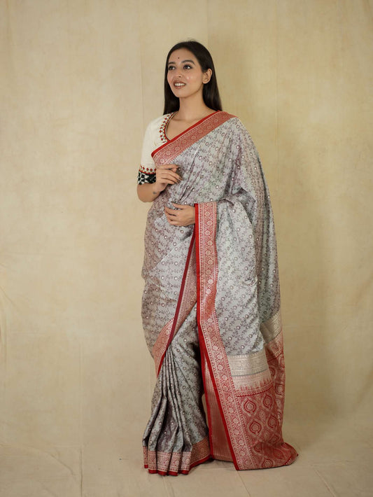 Grey semi Benarasi silk saree with intricate patterns and matching blouse piece from Joyee Kolkata, displayed on a plain background.