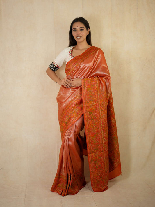 Reddish orange semi Benarasi silk saree with intricate designs, paired with a 1-meter matching blouse piece, by Joyee Kolkata.