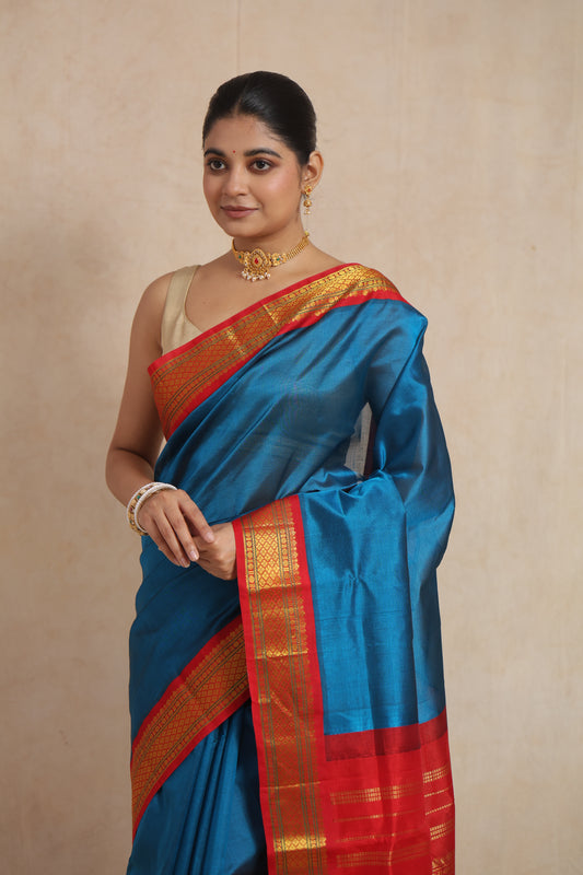 Close-up of a teal blue Kanchipuram Sico Saree by Joyee Kolkata with a crimson red zari border and intricate woven details.