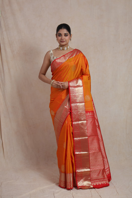 Model wearing sunset orange Kanjivaram silk saree with red zari woven pallu