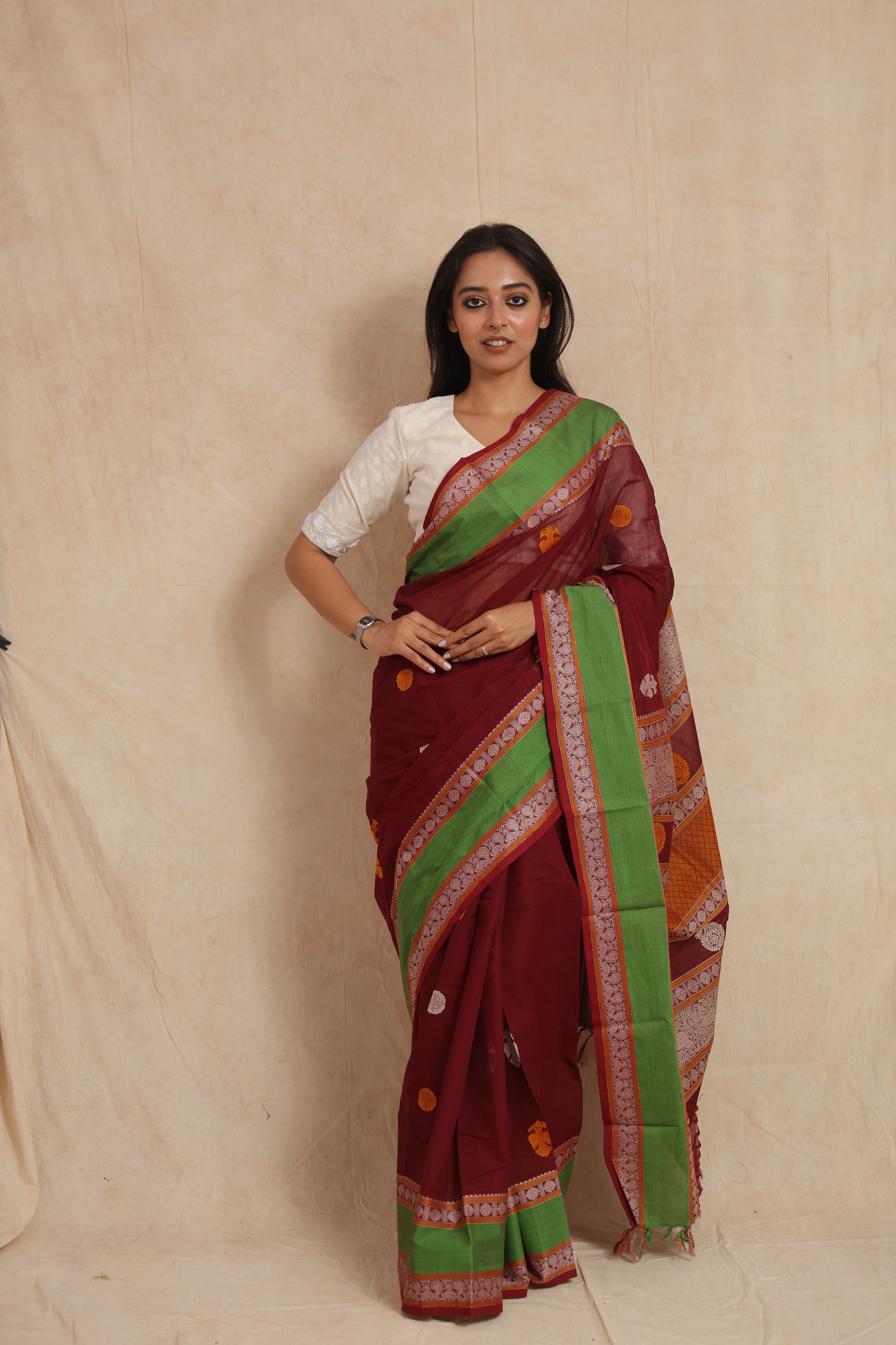 Front view of maroon Kanchipuram cotton saree with green border and traditional woven motifs