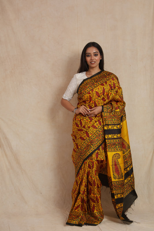 Model wearing mustard yellow Batik silk saree with intricate leaf motifs and traditional paisley pallu