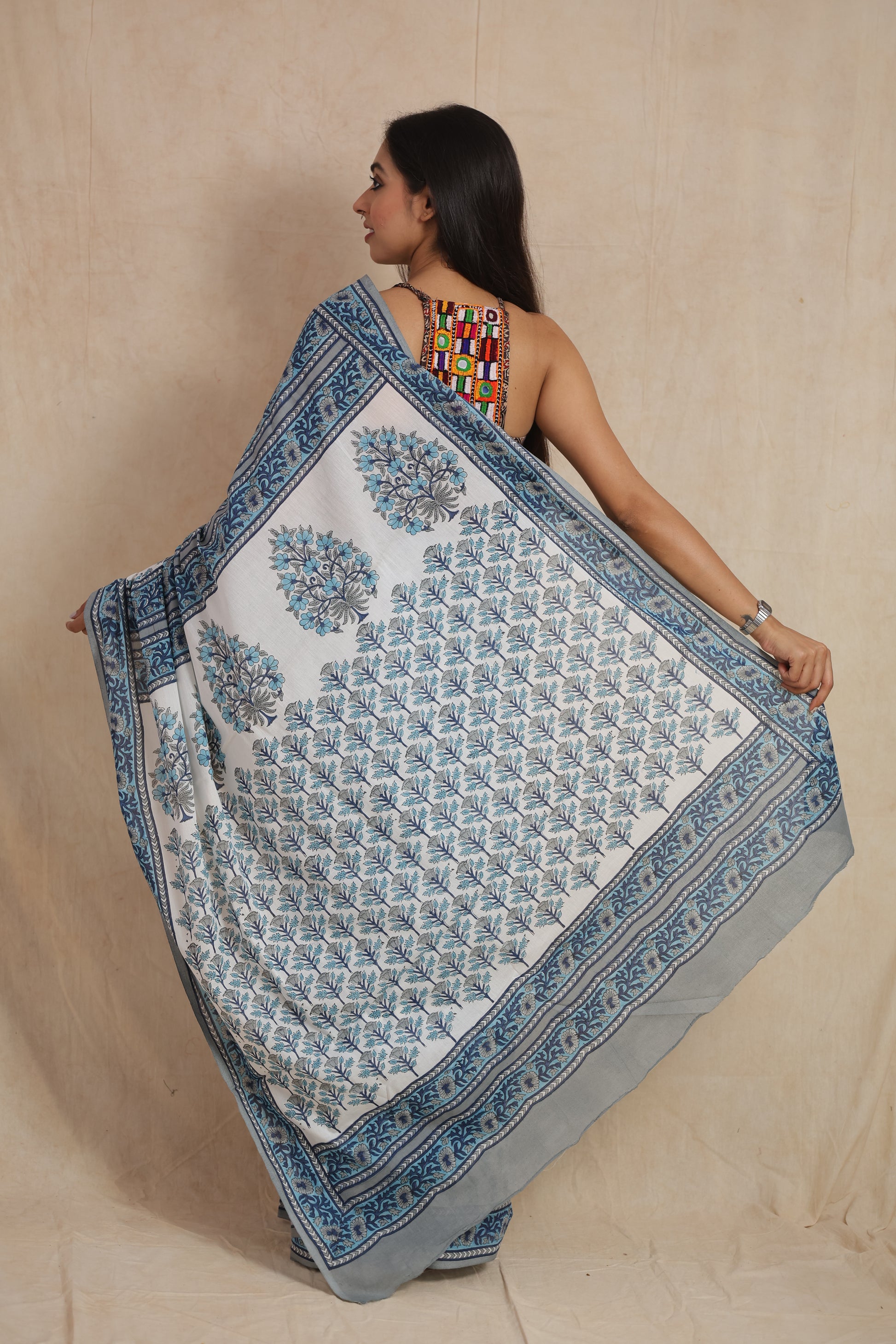 Back view of a white cotton saree showcasing the intricately printed blue floral pallu and border.