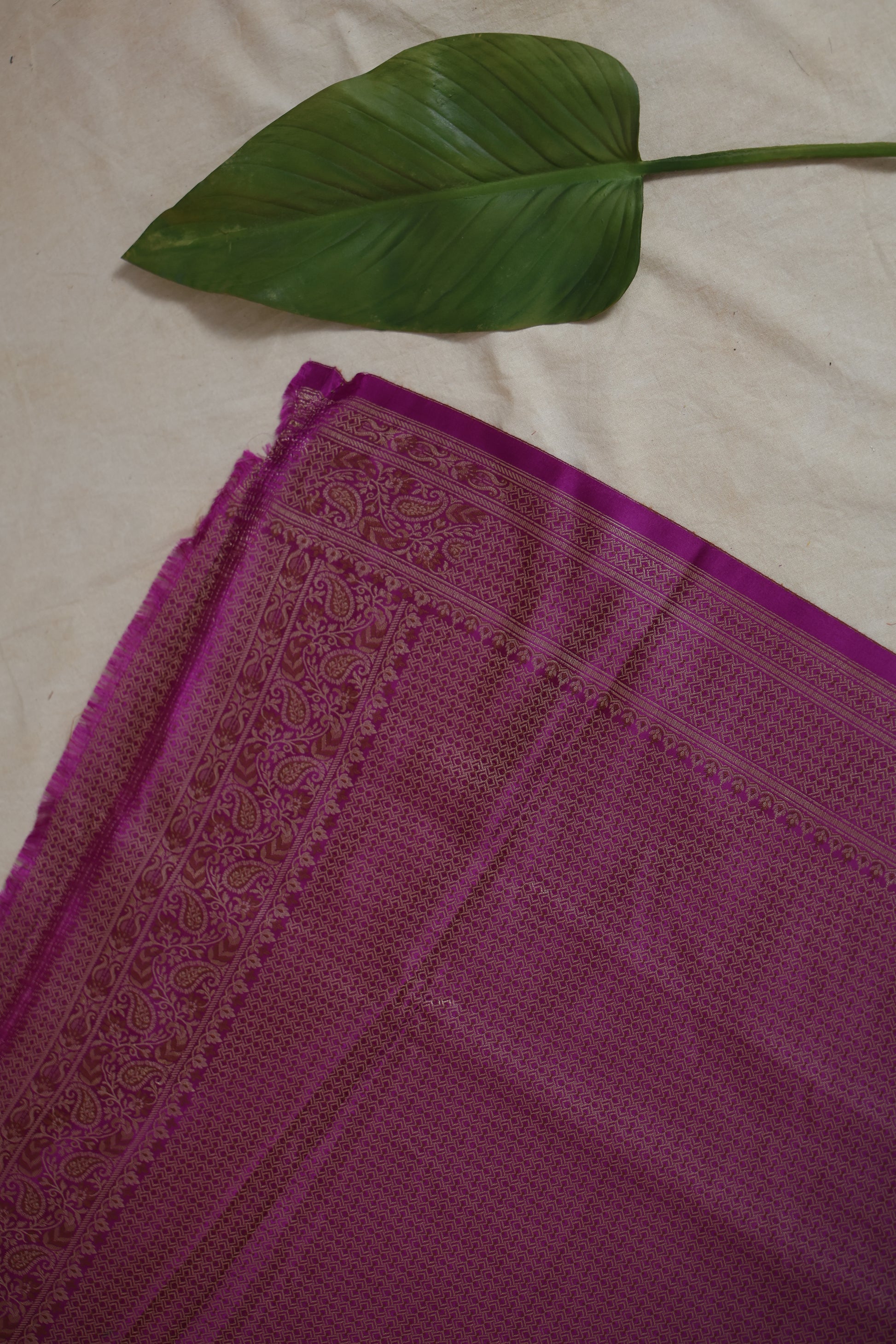 Flat lay of radiant magenta Banarasi silk saree displaying intricate woven border and texture