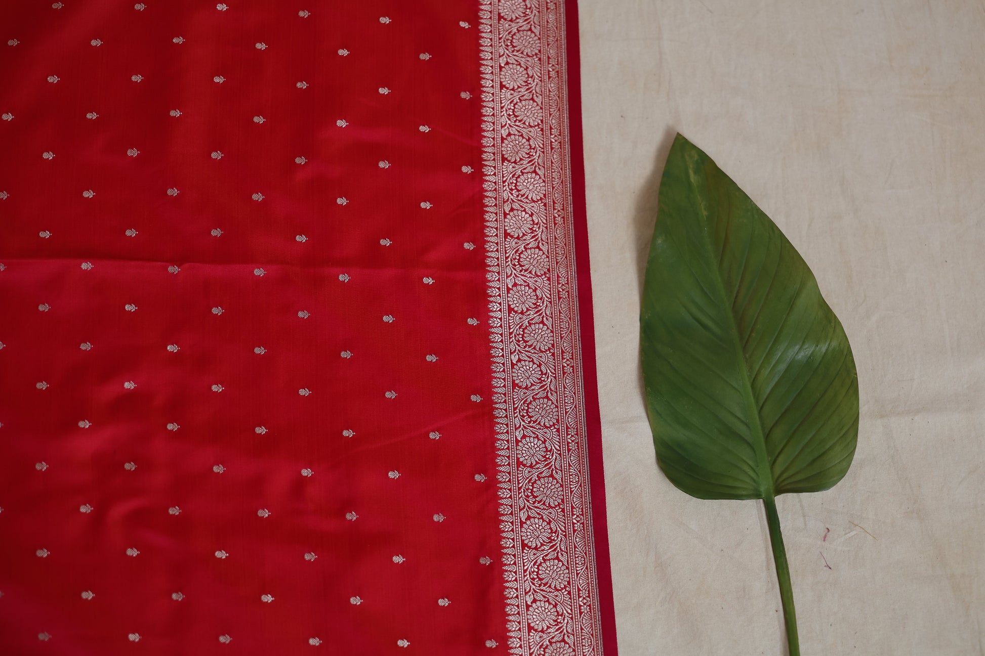 Flat lay of ruby red Banarasi silk saree highlighting silver zari buttas and border