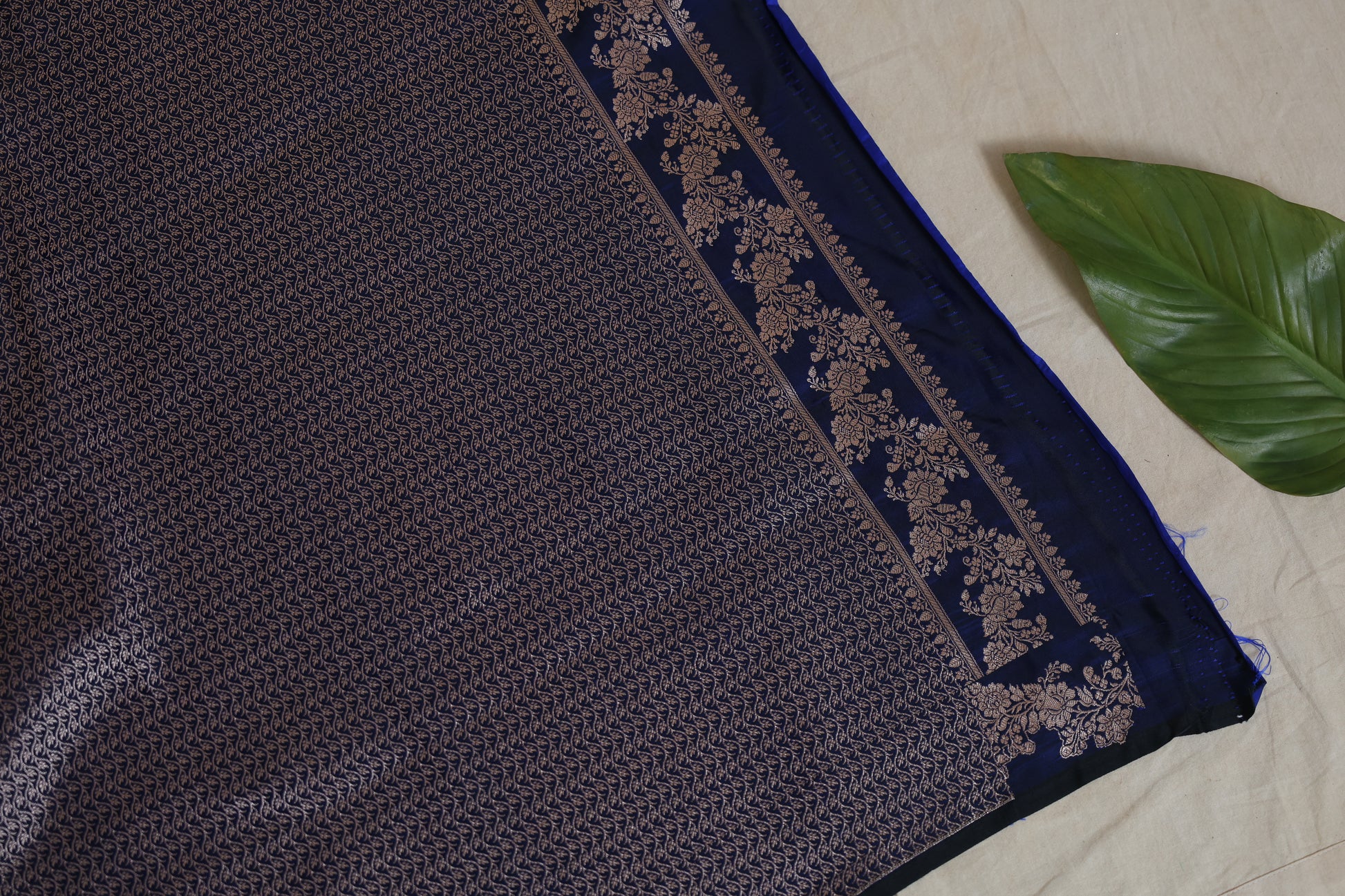 Flat lay view of royal navy blue Banarasi art silk saree with intricate woven floral border blouse.
