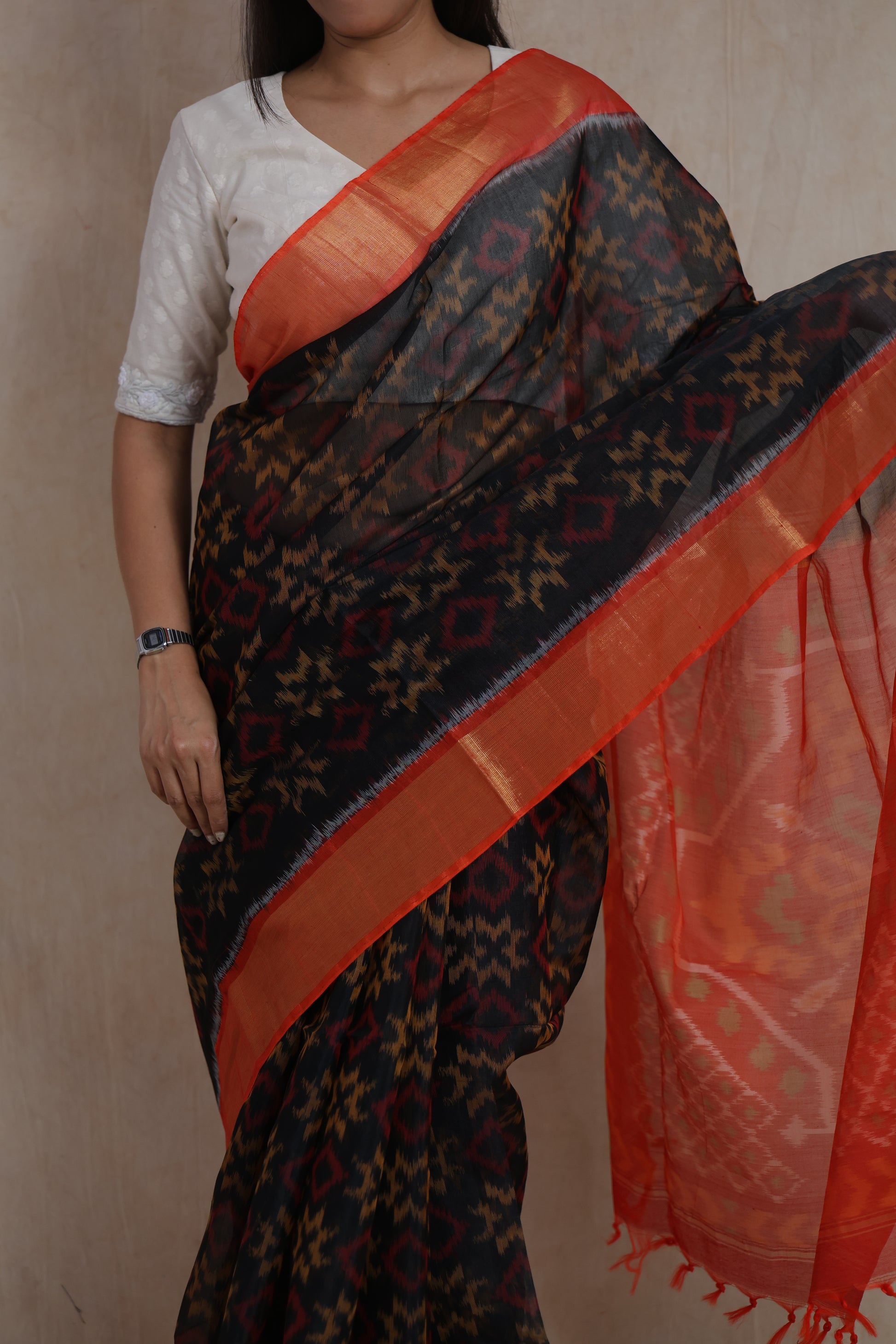 Portrait view of a handwoven black Pochampally SICO saree with orange border and traditional Ikat design.
