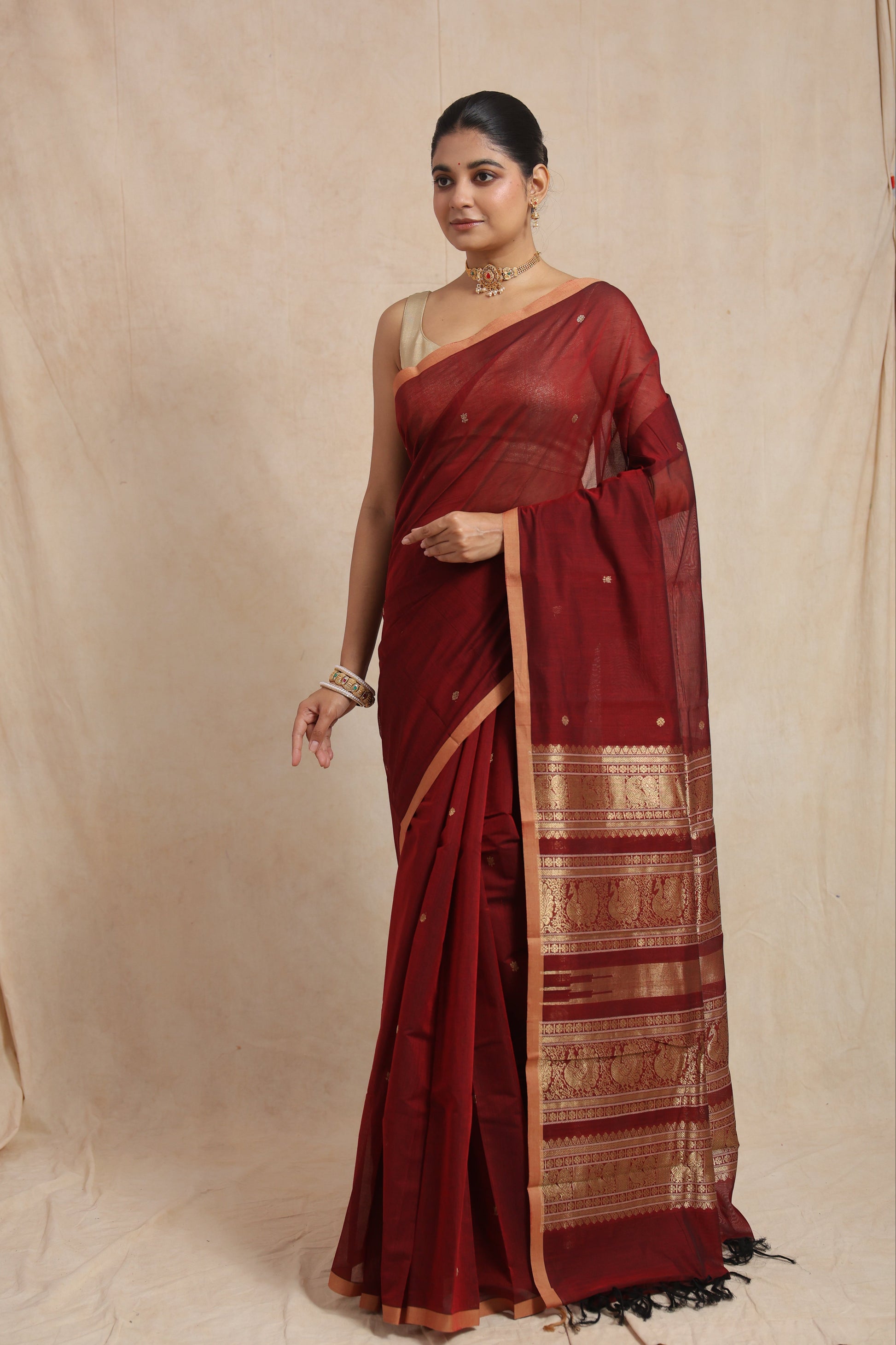 Front view of a maroon Kanchipuram cotton saree featuring delicate woven motifs, a copper-toned border, and a traditional pallu.
