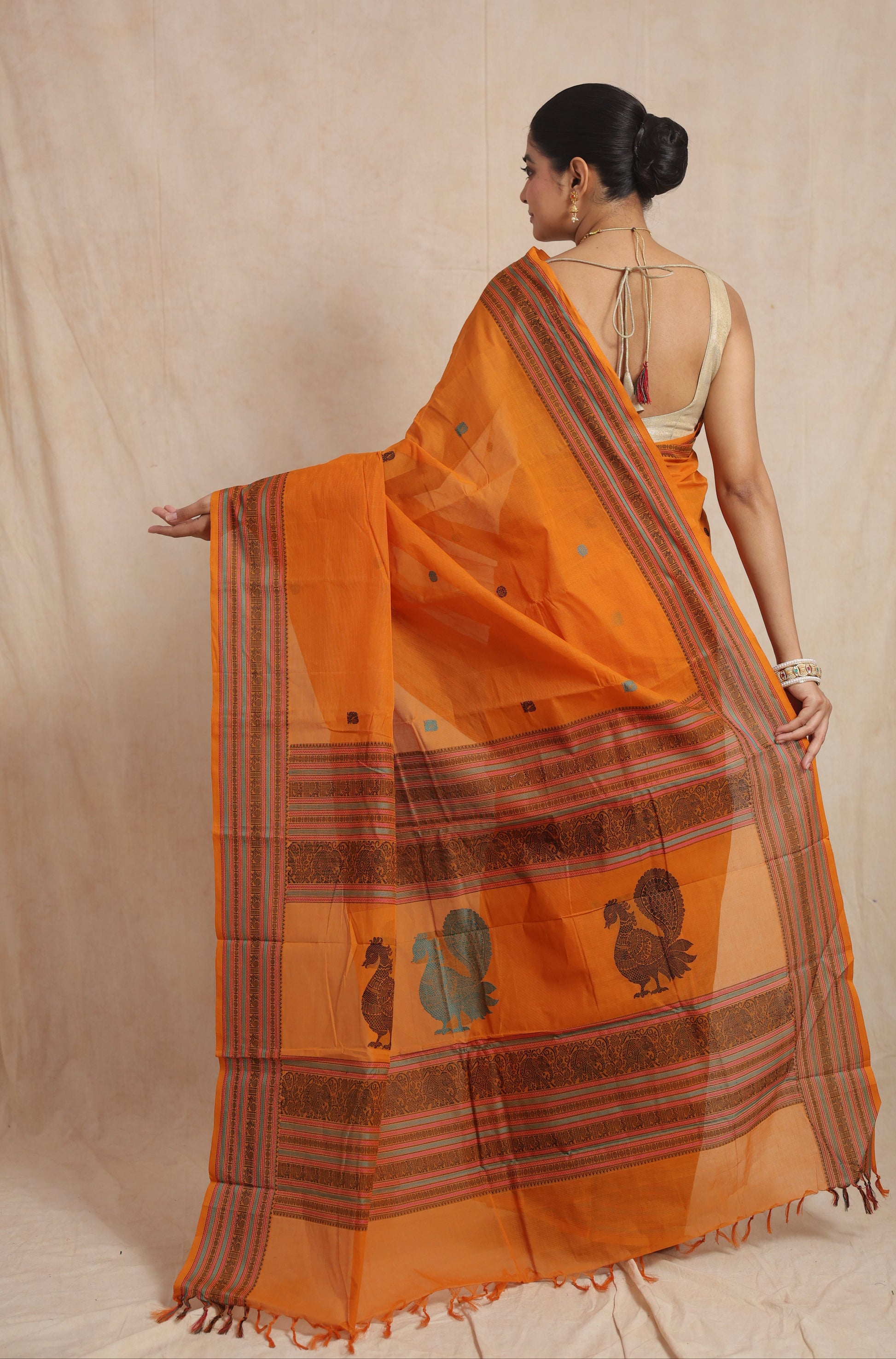 Back view of orange Kanchipuram cotton saree showcasing artistic peacock motif pallu