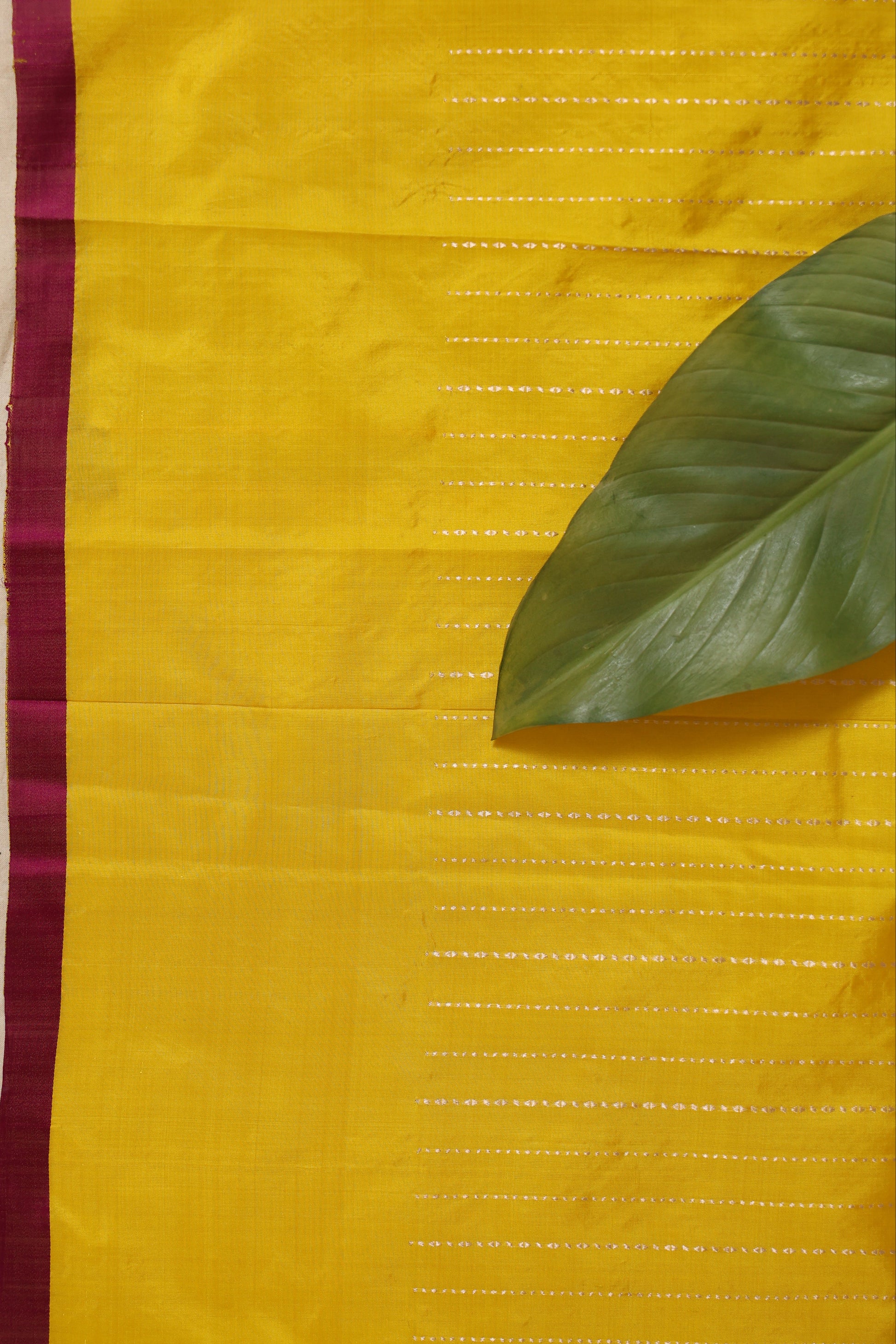 Flat lay of sunshine yellow Banarasi silk saree displaying woven texture and border
