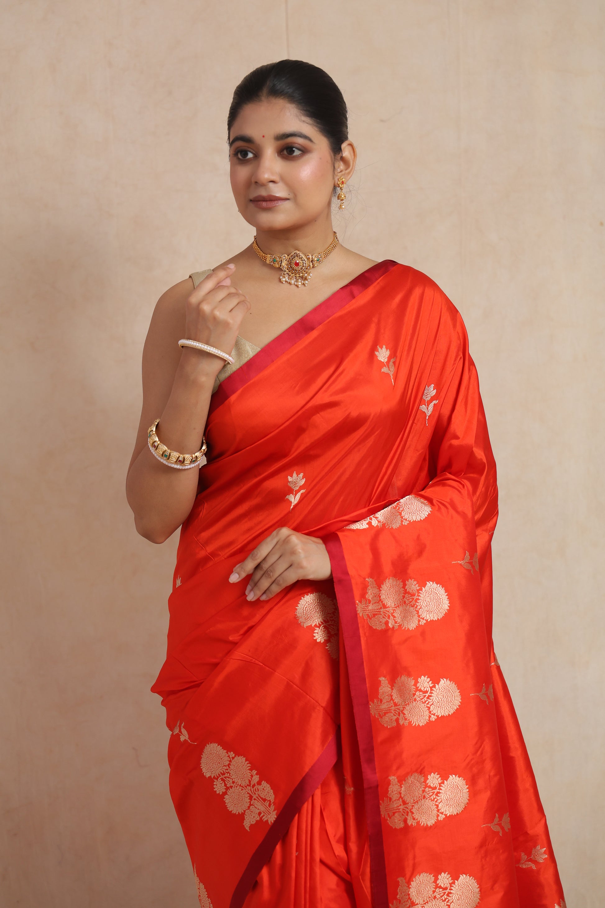 Model wearing vibrant vermilion Banarasi silk saree with floral woven motifs