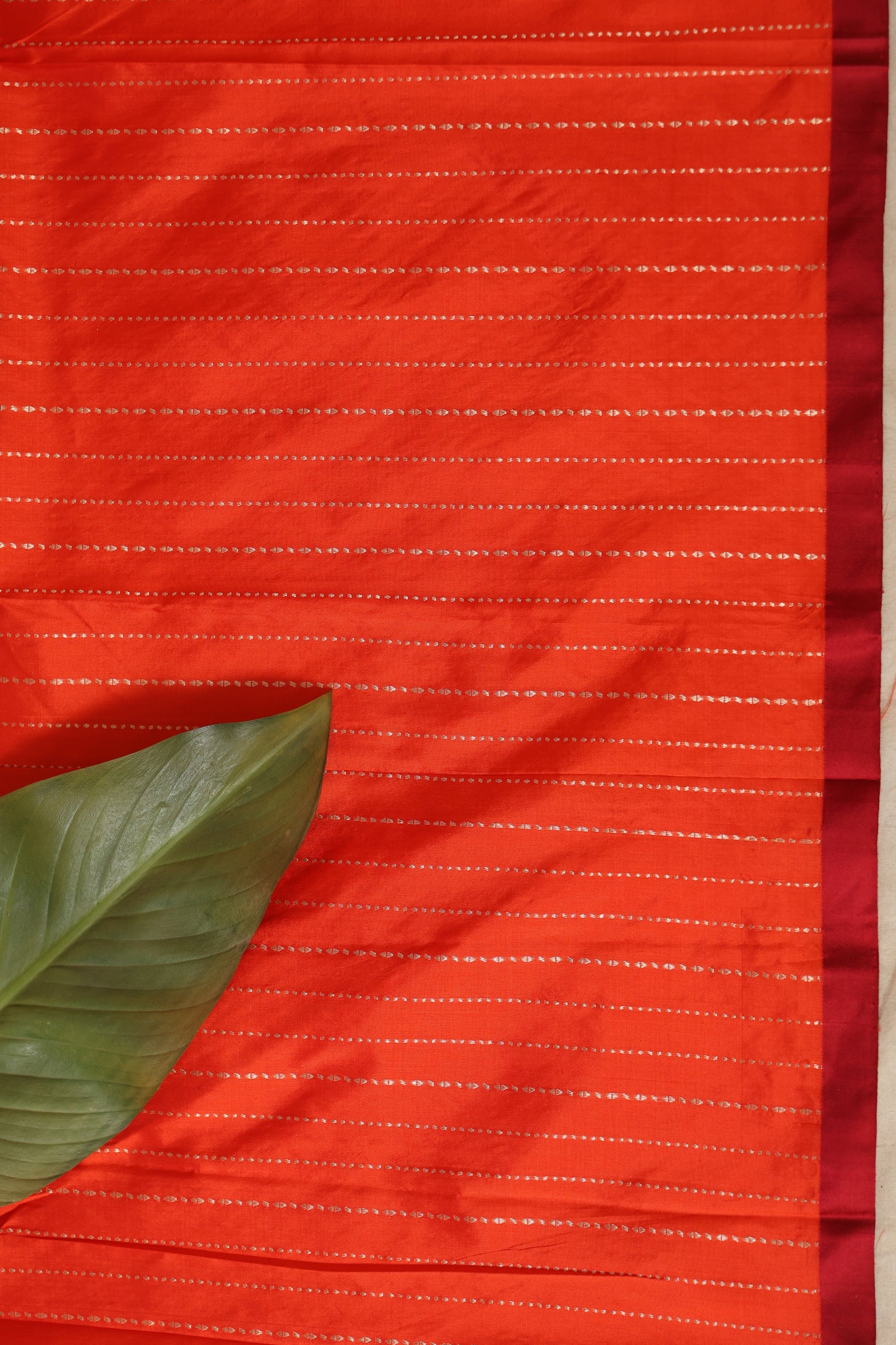 Flat lay of vibrant vermilion Banarasi silk saree displaying woven texture and border