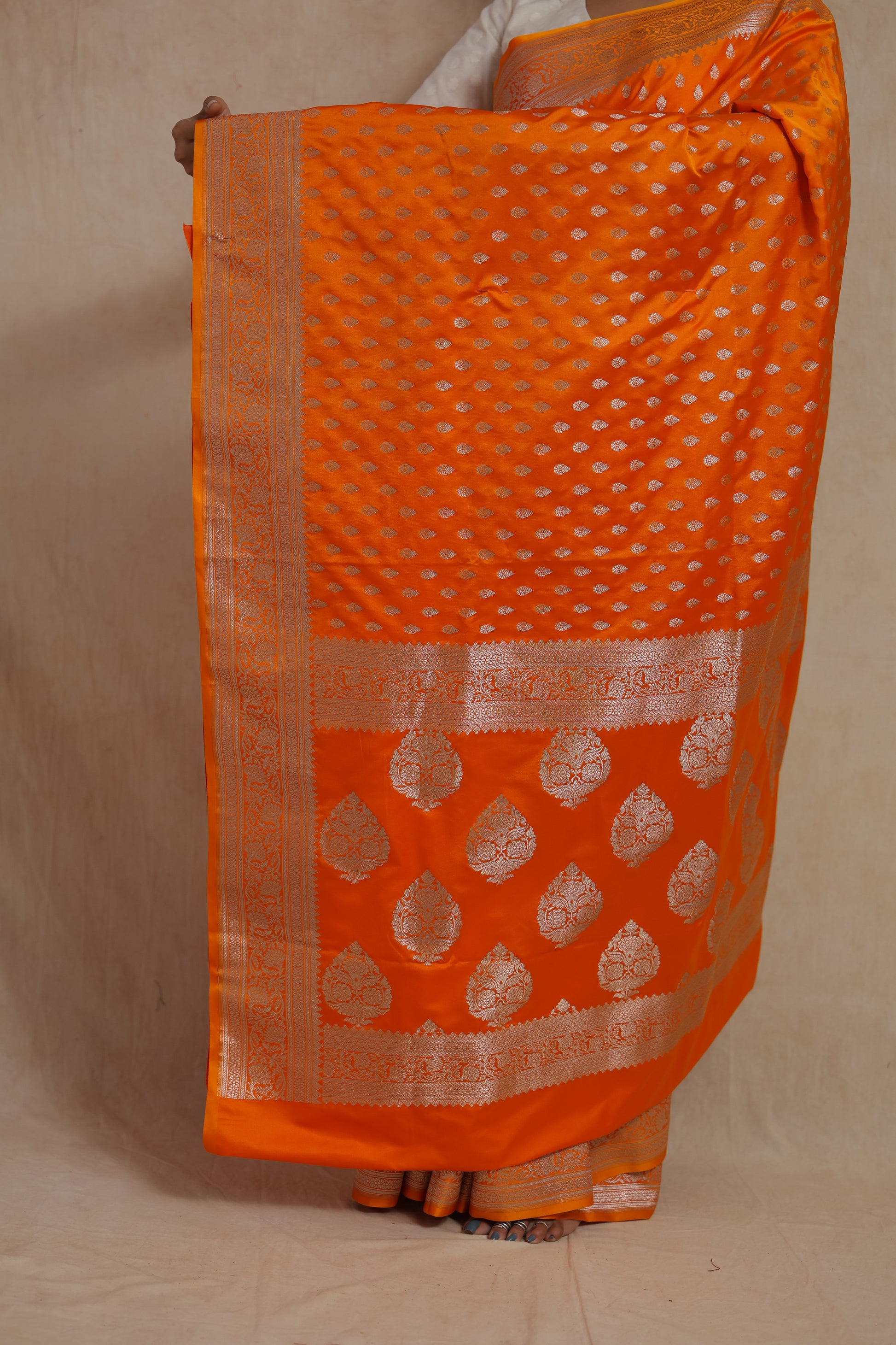 Close-up of richly woven pallu and silver zari motifs on orange silk saree.