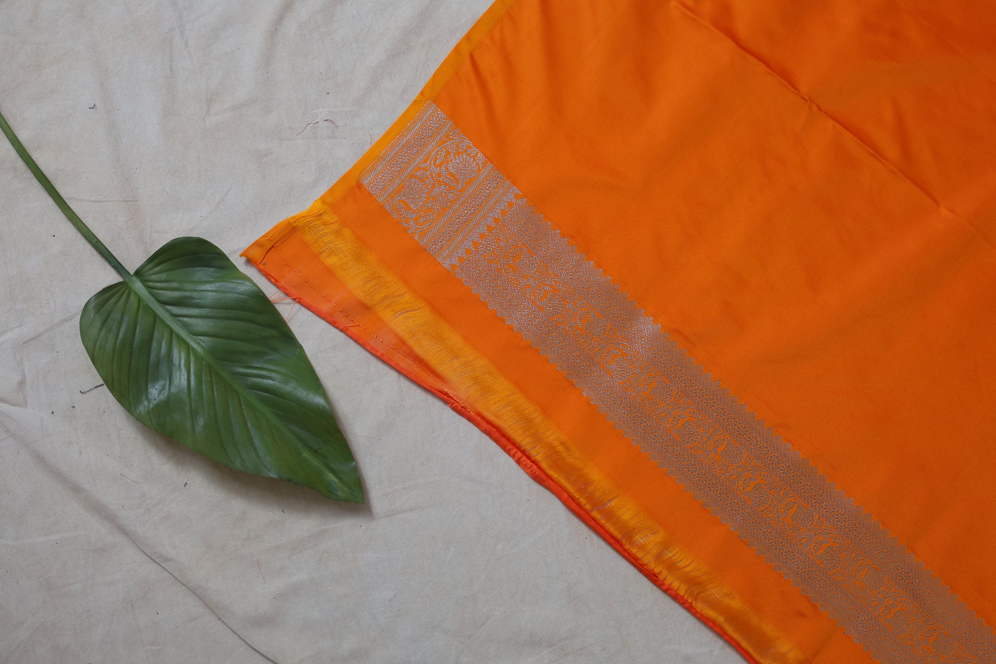 Detailed pallu shot featuring intricate silver zari craftsmanship on orange saree.