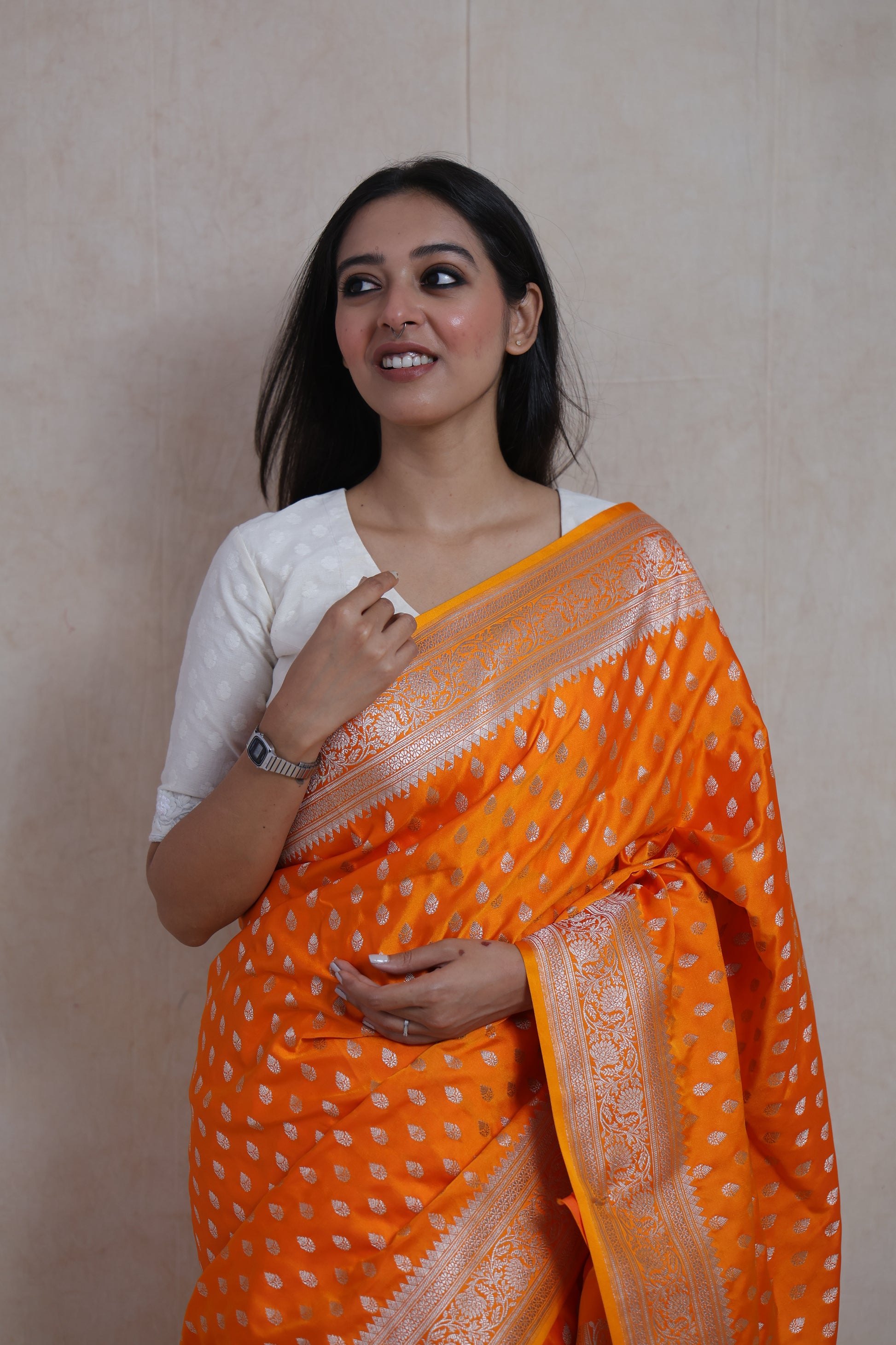 Portrait shot of model in luxurious orange Banarasi saree with zari border.