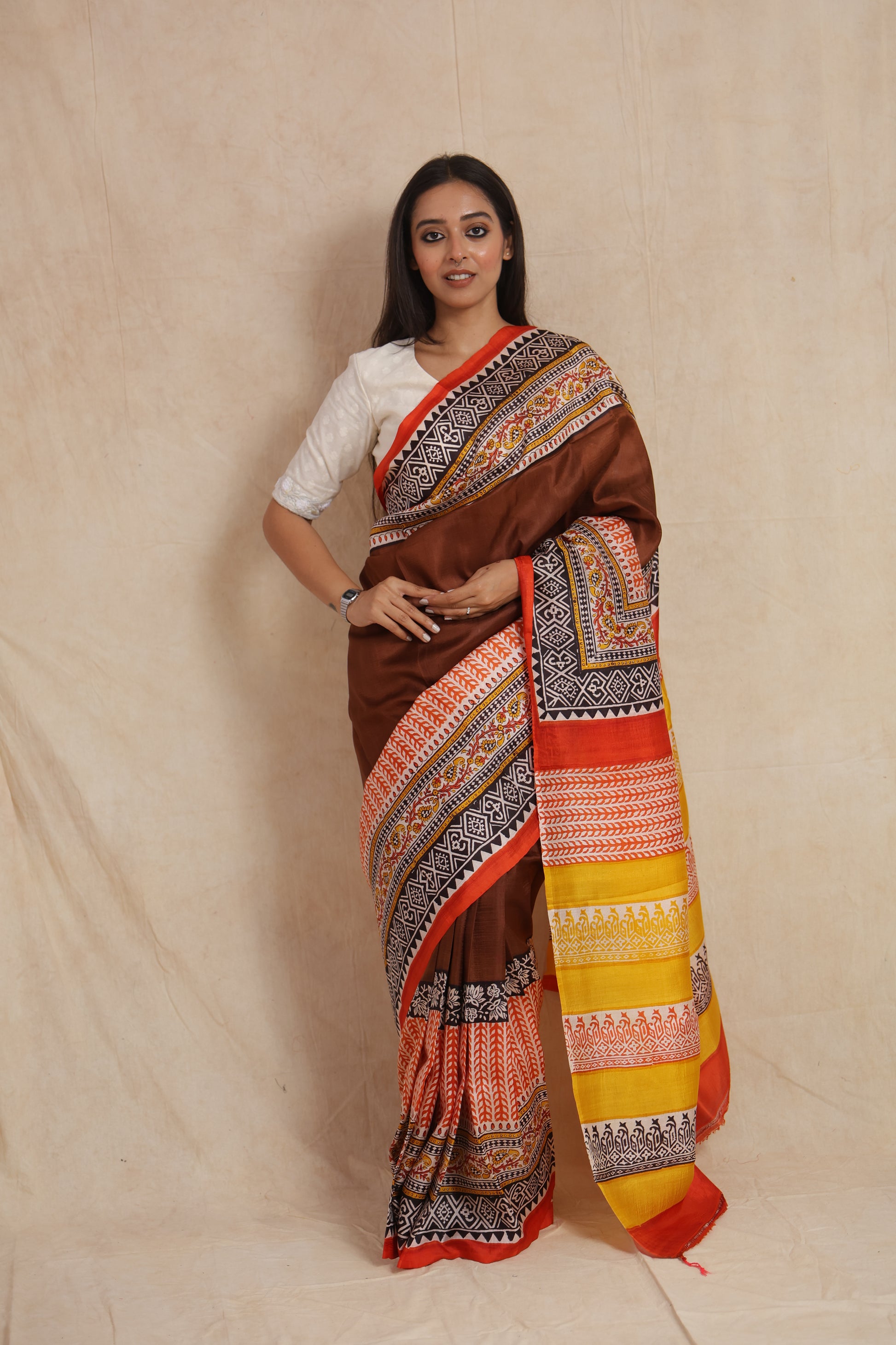 Model wearing chocolate brown Batik silk saree with intricate traditional borders and mustard yellow pallu