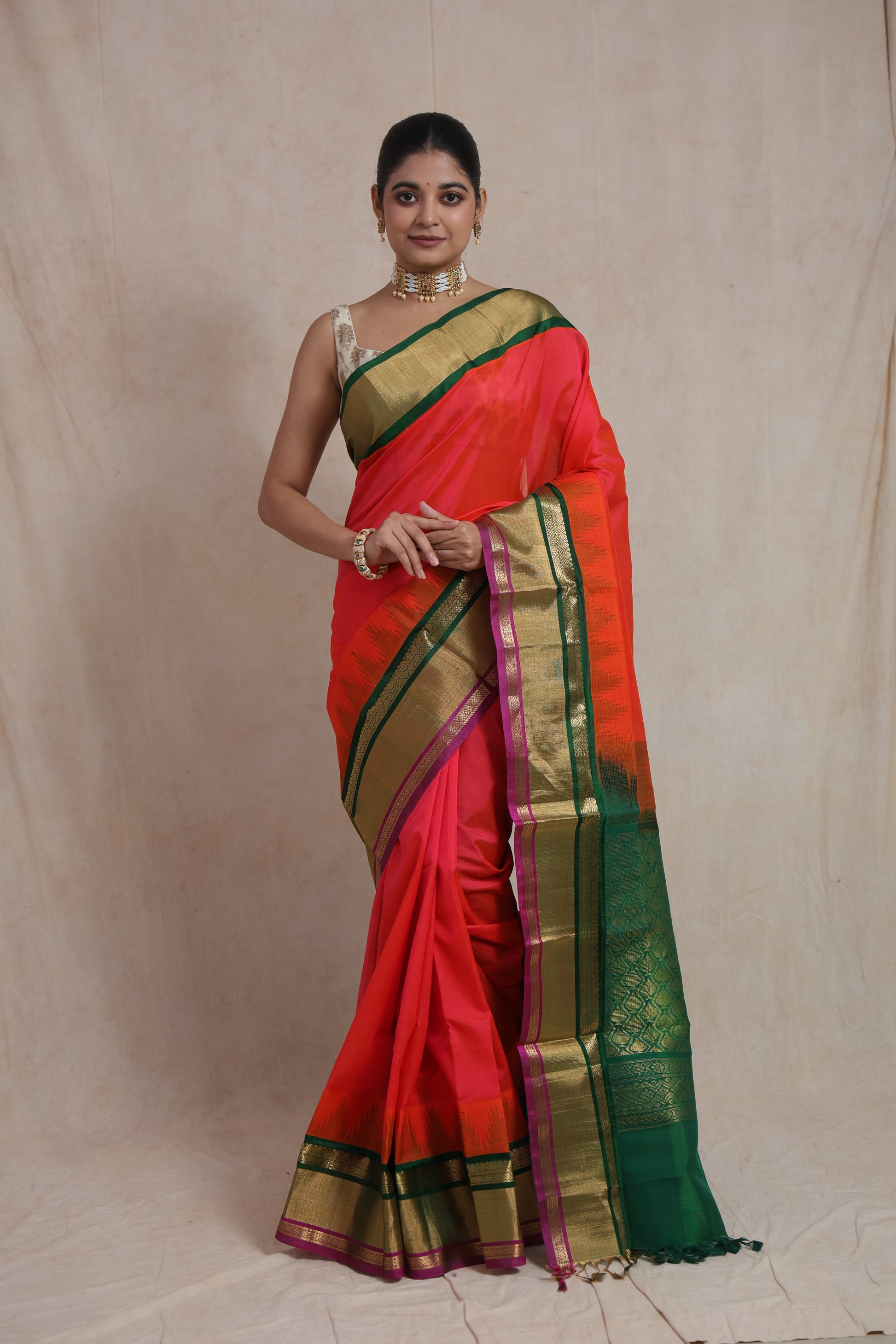 Model wearing coral red Kanchipuram silk cotton saree with emerald green zari border