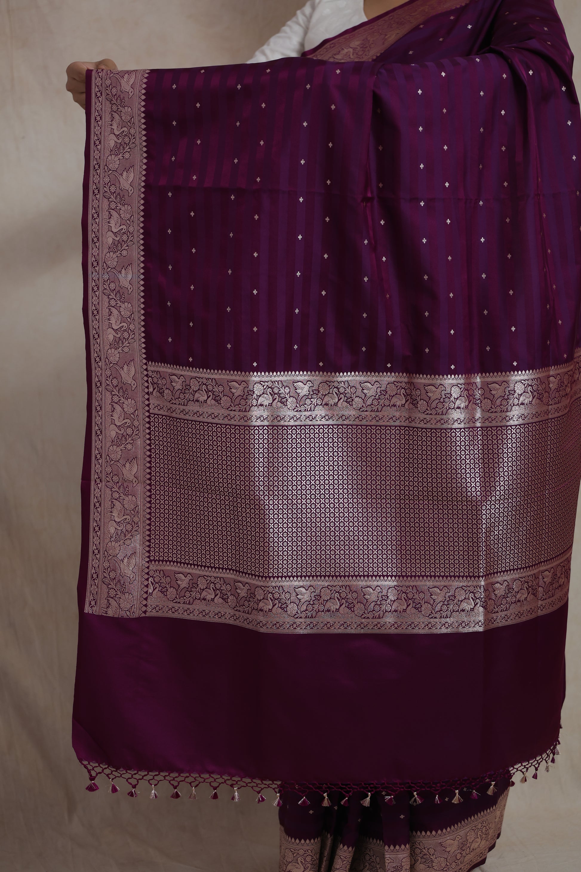 Close-up of detailed silver zari woven pallu and floral border on wine silk saree.