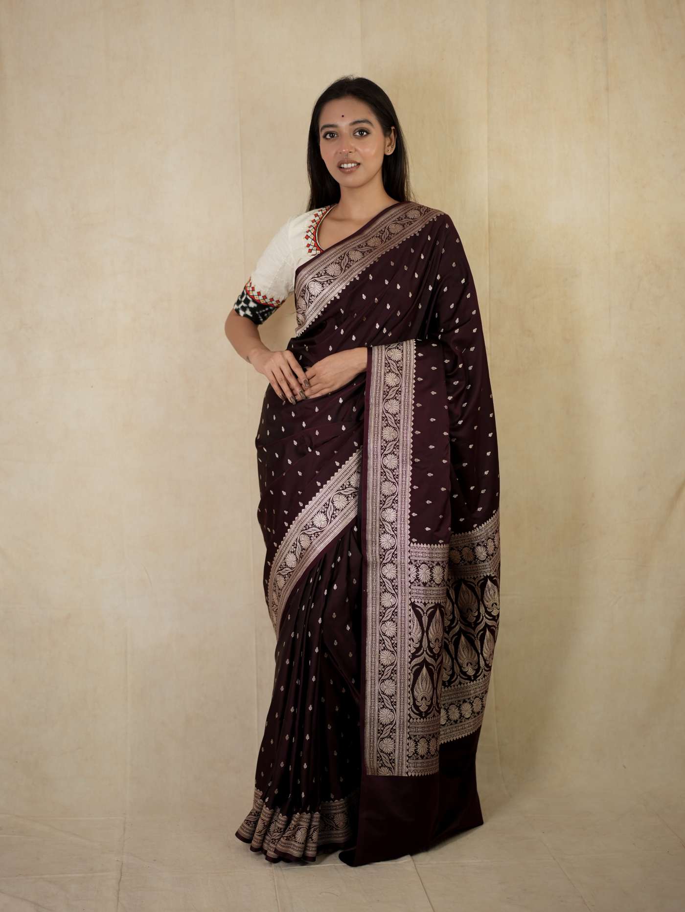 Dark brown Benarasi semi-silk saree with intricate zari work and matching blouse piece, displayed on a hanger.