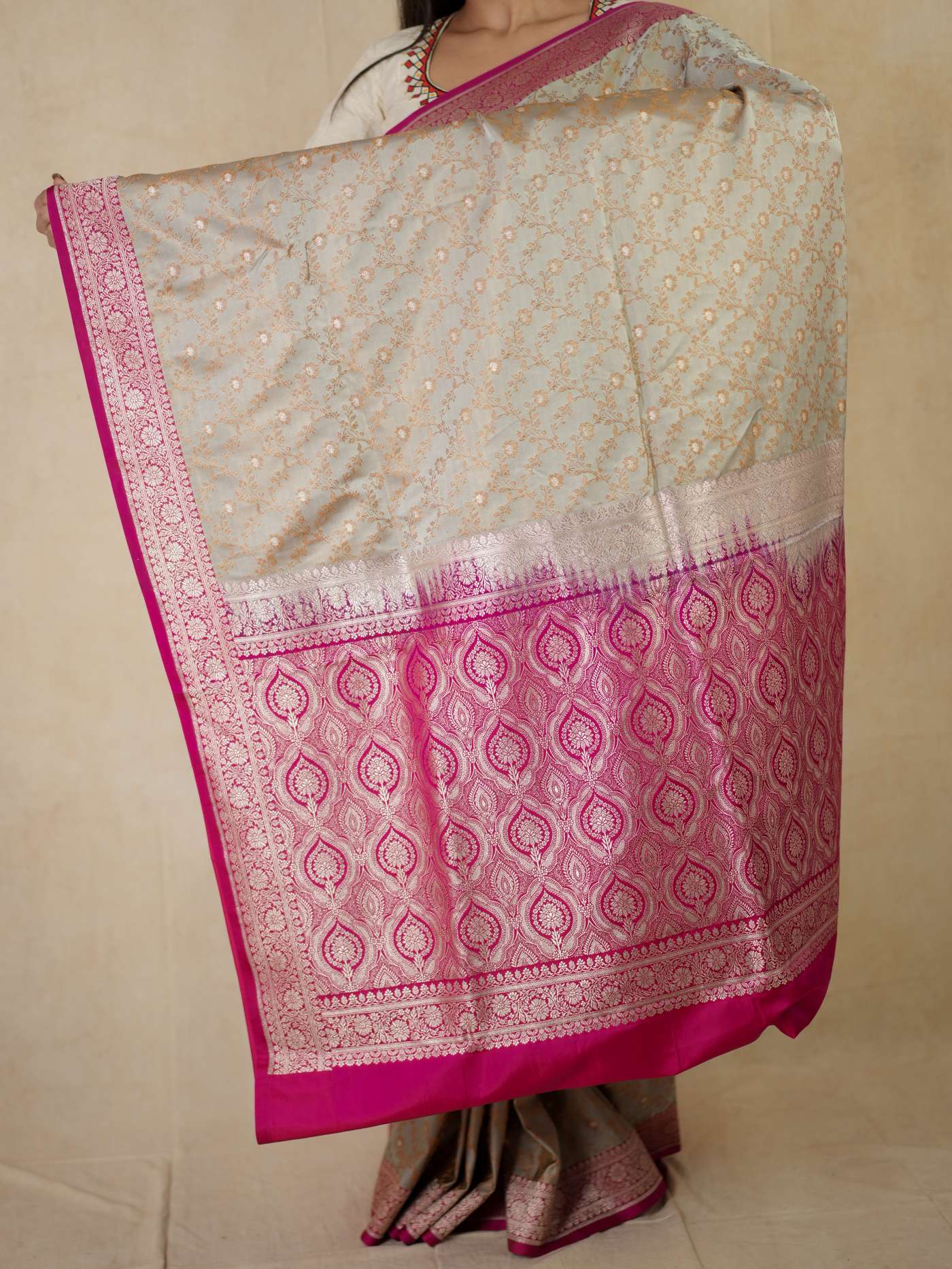 Gray semi-Benarasi silk saree with intricate patterns and matching blouse piece from Joyee Kolkata, displayed on a hanger.