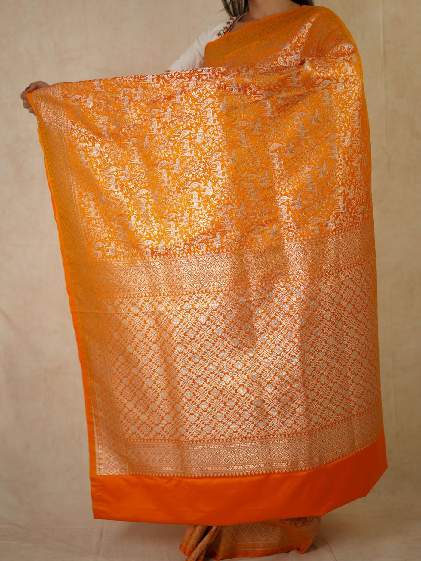 Orange semi-Benarasi silk saree with intricate designs and matching blouse piece from Joyee Kolkata, displayed draped on a mannequin.
