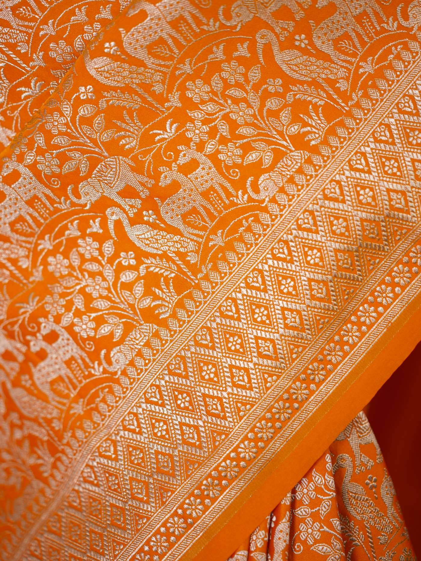 Orange semi-Benarasi silk saree with intricate design and matching 1 meter blouse piece by Joyee Kolkata, shown draped.