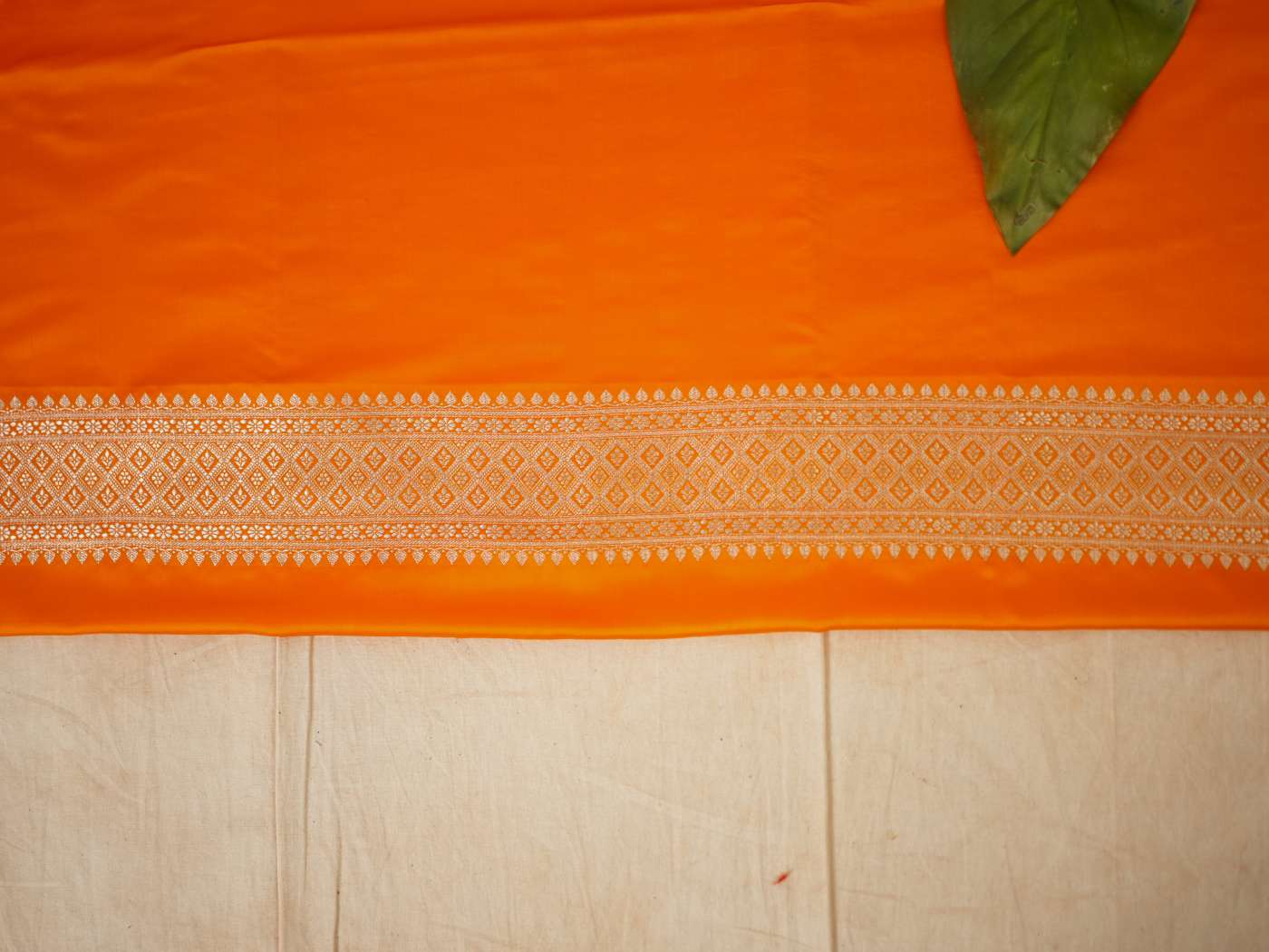 Orange semi-benaras silk saree with intricate patterns and matching blouse piece from Joyee Kolkata, displayed on a hanger.