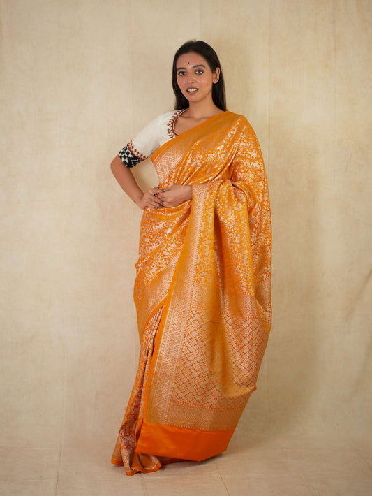 Orange semi-Benarasi silk saree with intricate designs and matching blouse piece from Joyee Kolkata, displayed on a mannequin.
