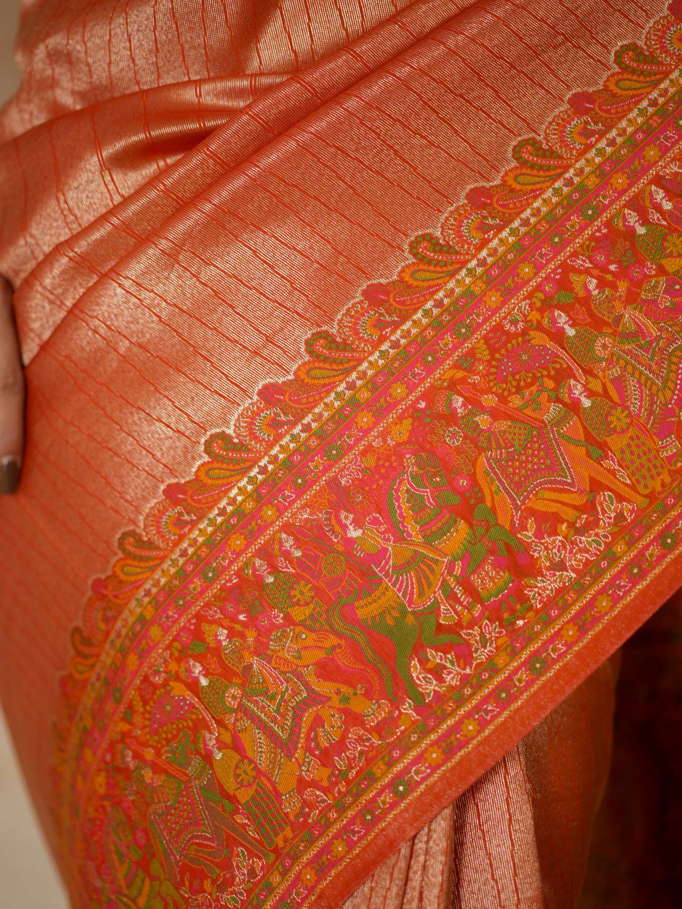 Reddish orange semi Benarasi silk saree with intricate designs and matching blouse piece by Joyee Kolkata, draped beautifully.