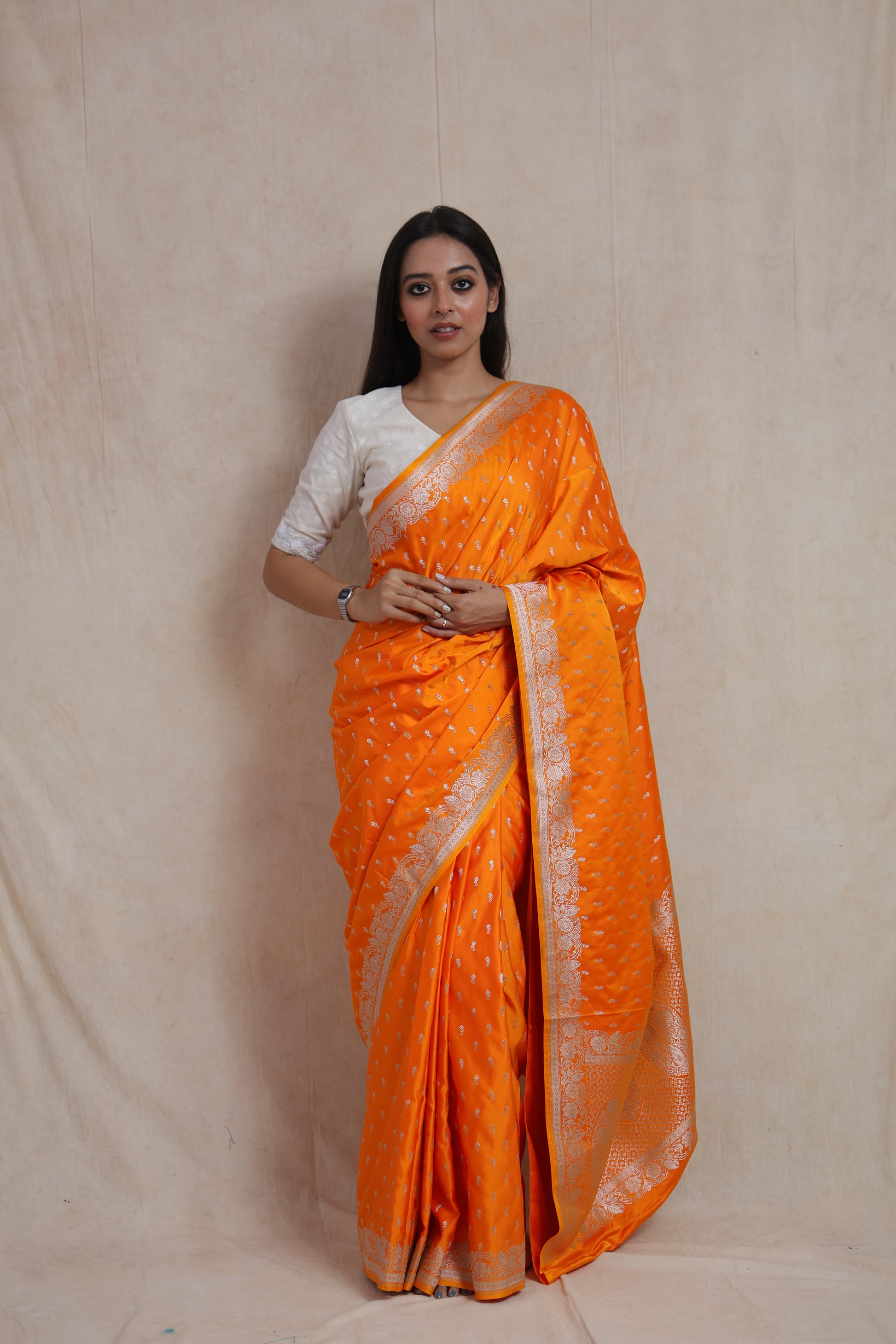 Front view of sunlit orange Banarasi silk saree with silver woven buttas and floral border