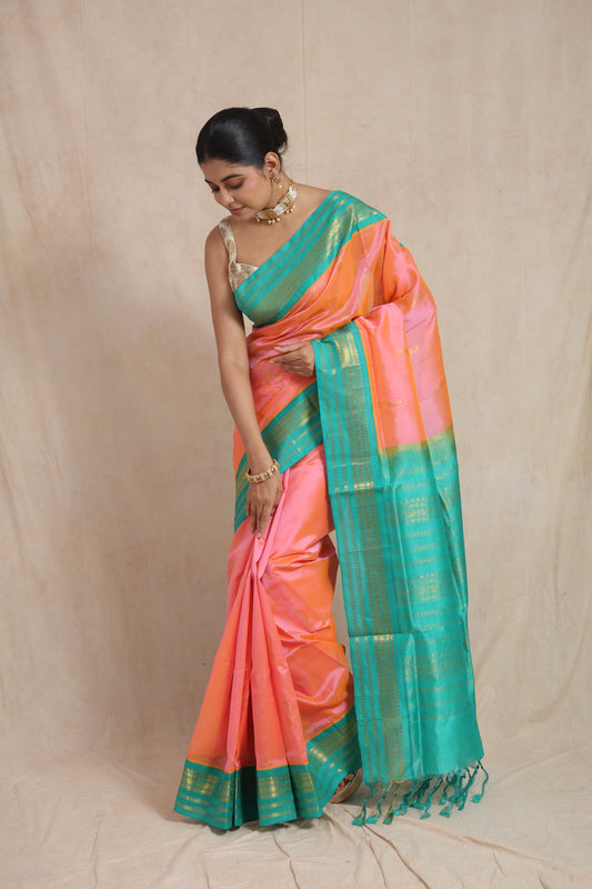 Styled pose of elegant peach pink Kanchipuram Sico saree with aqua blue border