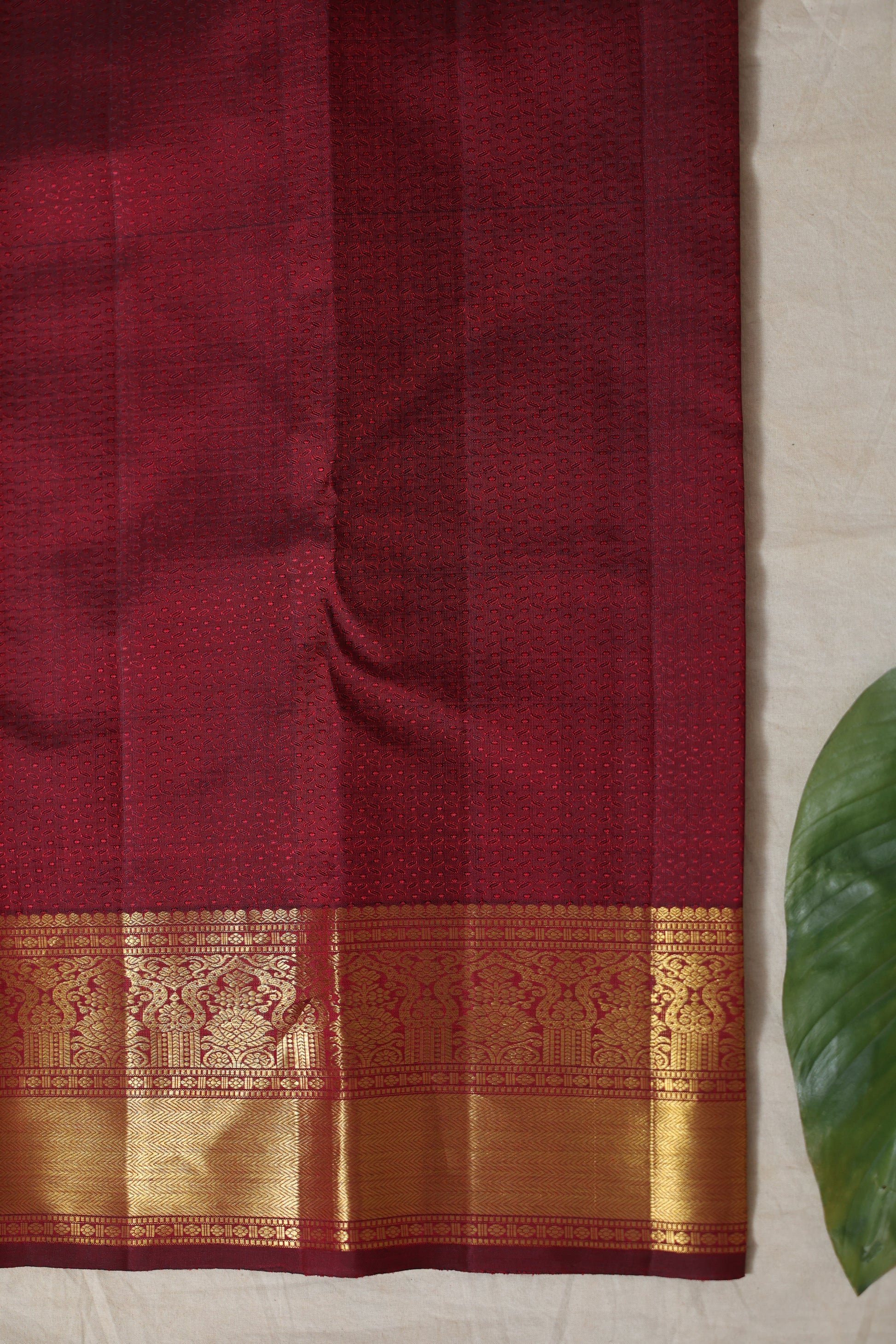 Flatlay view of maroon Kanjivaram silk saree with rich zari woven border