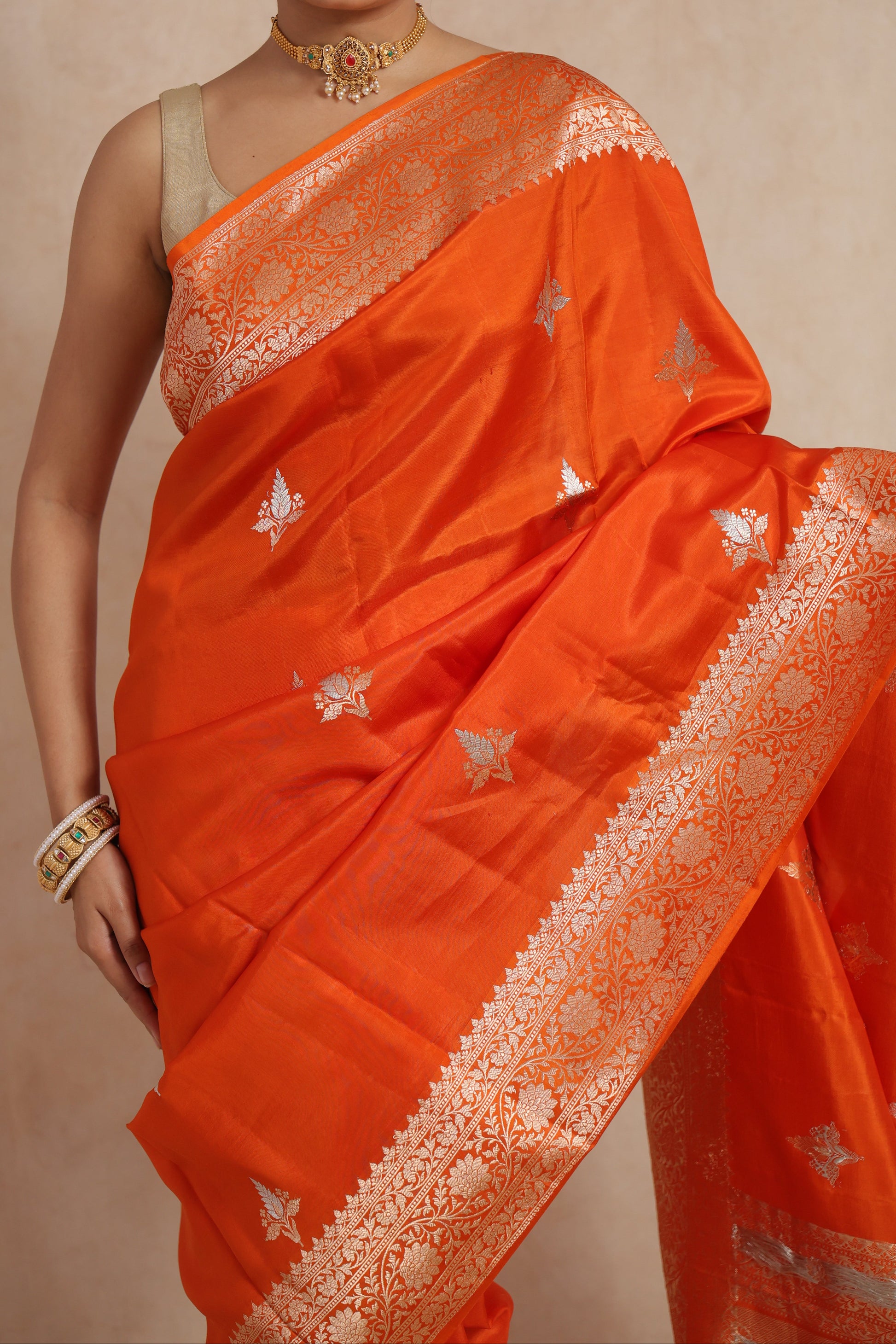 Close-up of orange Banarasi silk saree featuring intricate floral border and woven motifs