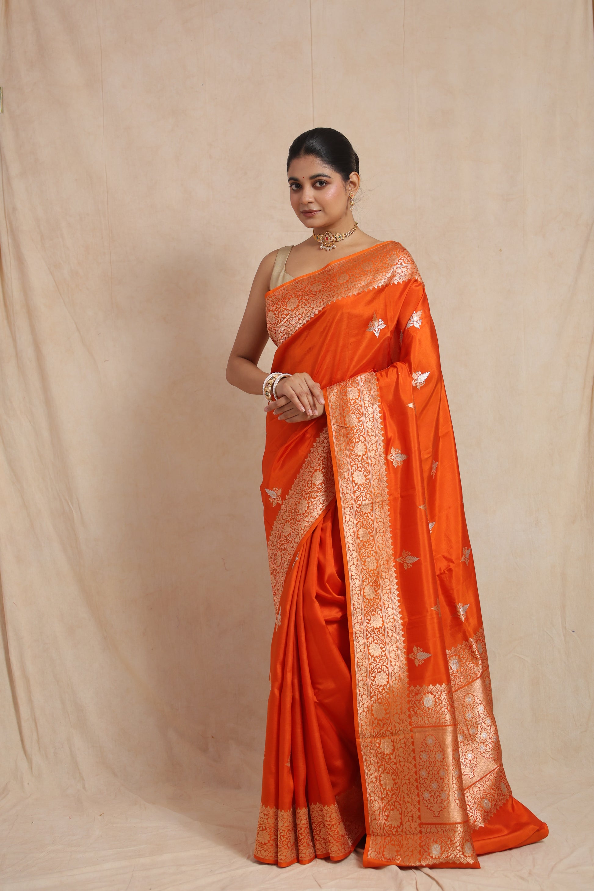Front view of radiant tangerine orange Banarasi silk saree with floral woven border and traditional buttas