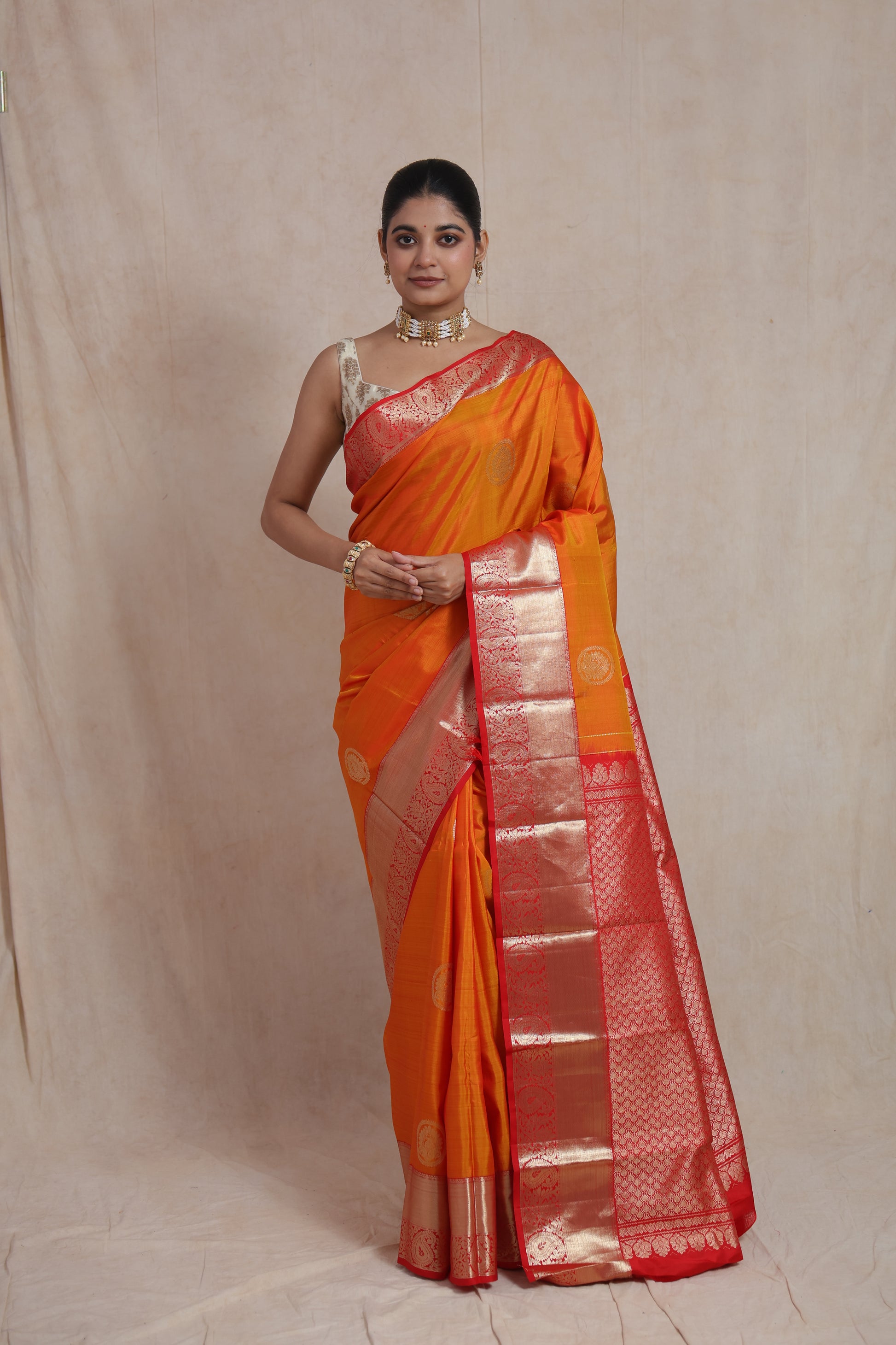 Model wearing sunset orange Kanjivaram silk saree with red zari woven pallu