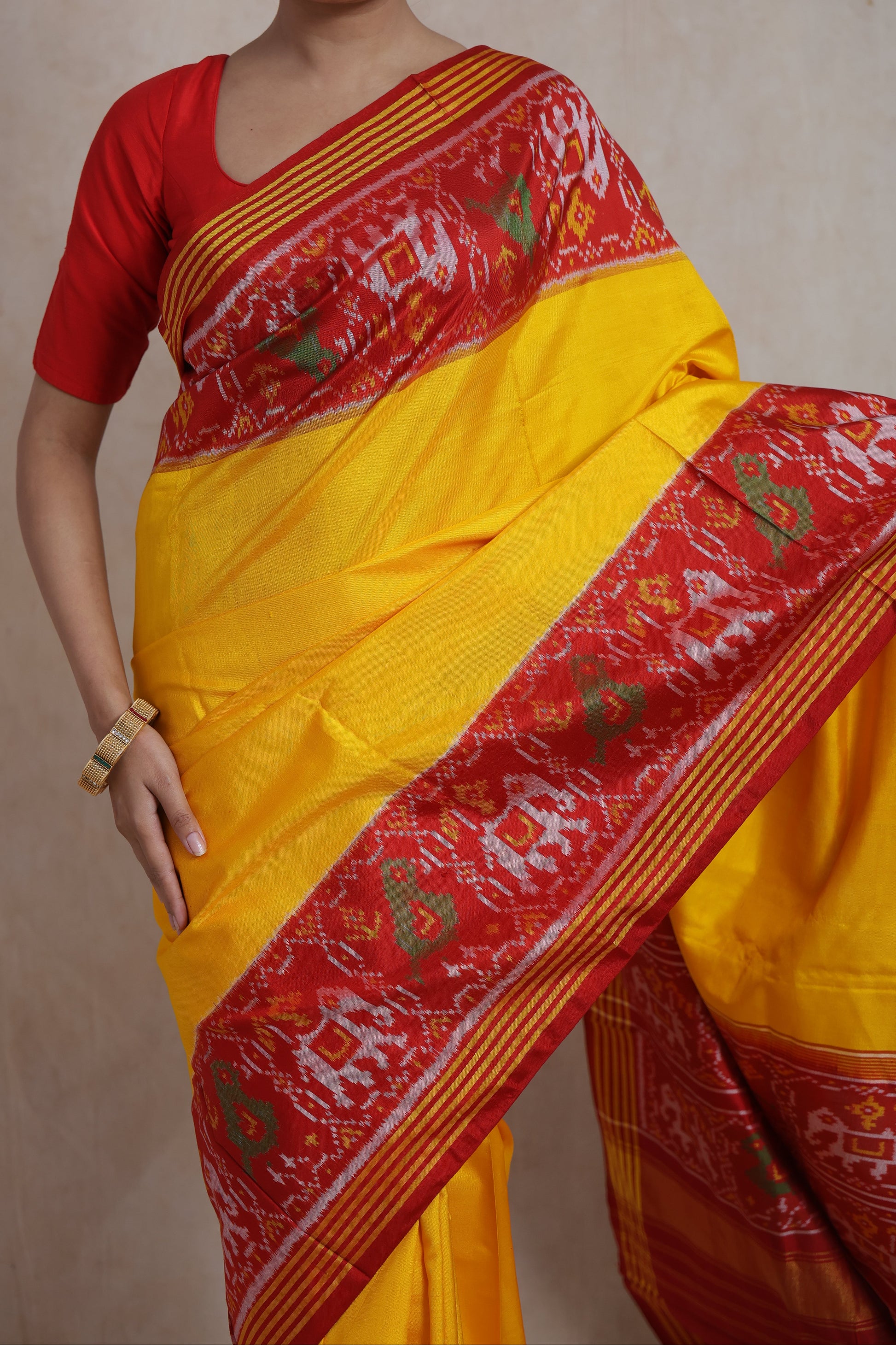 Close-up of sunshine yellow Patola silk saree featuring red woven border with traditional ikat and bird motifs